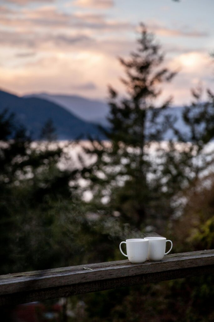 pexels-photo-3932951-3932951 Serene landscape view with two coffee mugs on a wooden railing at sunset.